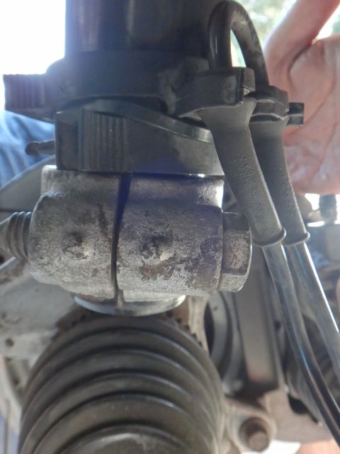1995 Ford Taurus - A close-up view of a rusty suspension component with attached hoses, likely from a vehicle's steering or suspension system.