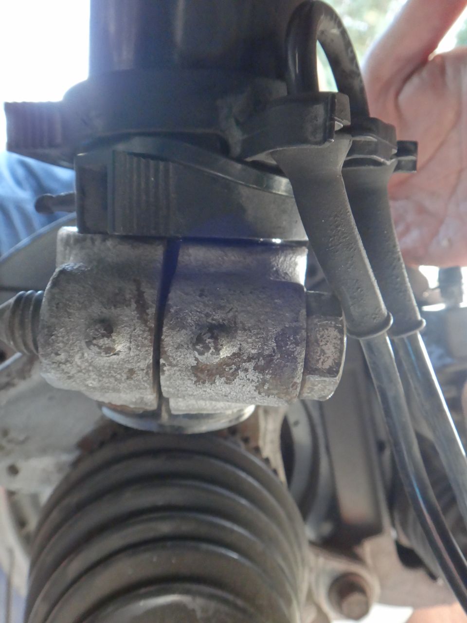 Close-up of a rusty metal suspension part with two black hoses attached