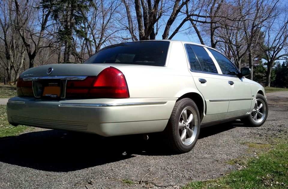 Champagne Mercury Grand Marquis sedan parked among bare trees