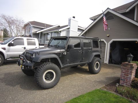 2008 Jeep Wrangler - A black Jeep Wrangler is parked in a driveway, showing its modified exterior and large tires.