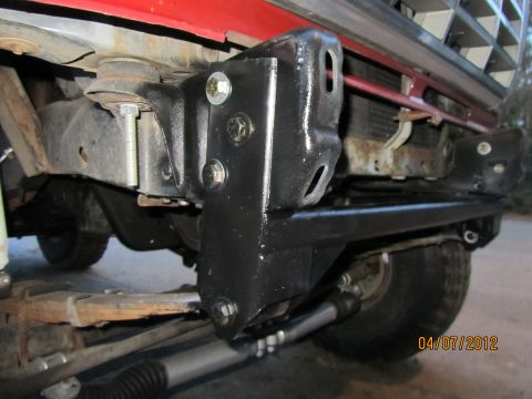 1984 Ford Bronco - Close-up of a red Ford Bronco's front bumper mount, showing modifications and hardware.