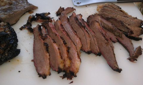 1989 Ford Bronco - A close-up view of sliced brisket, some pieces charred, arranged on a white cutting board.