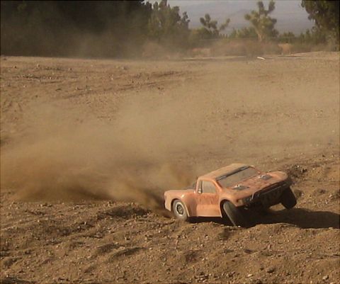 1996 Ford Bronco - An orange remote-controlled truck kicks up a cloud of dust as it drifts on a dirt track.