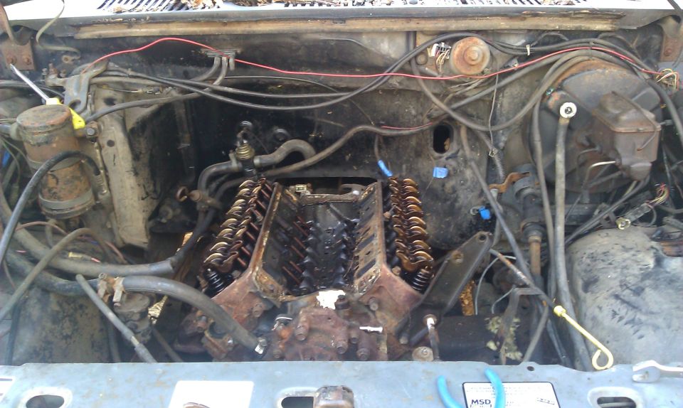 Engine bay with V8 engine exposed, wires and hoses visible