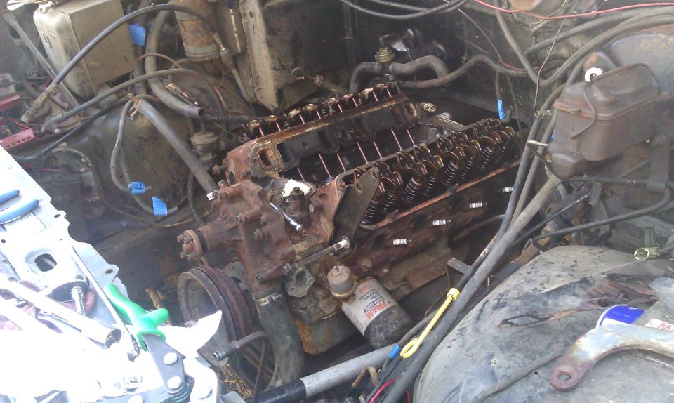 Engine bay showing a V8 engine with valve covers removed, oil filter visible. Tools are on the left