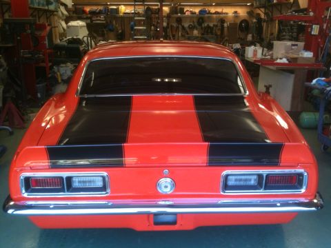 1968 Chevrolet Camaro - Rear view of a red 1968 Chevrolet Camaro with black racing stripes, parked in a garage.
