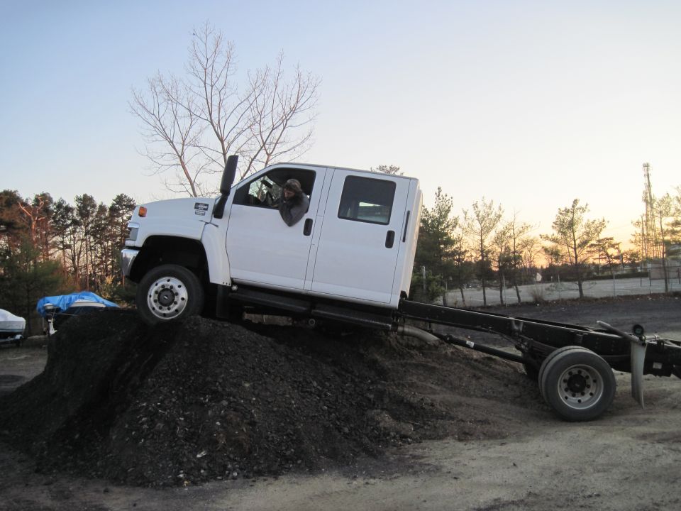 White crew cab truck chassis with a driver, angled on a dirt mound