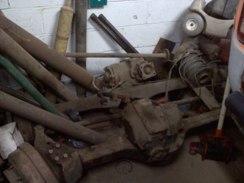 1978 Ford Bronco - Various rusty vehicle drivetrain parts are stored together in a cluttered garage setting.