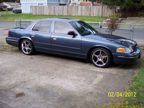 1998 Ford Crown Victoria - A blue 1998 Ford Crown Victoria is parked on a concrete driveway in front of a wooden fence.