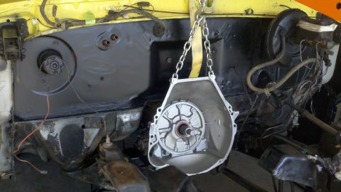 1978 Ford Bronco - A transmission is suspended by chains, undergoing removal from a vehicle's engine bay.