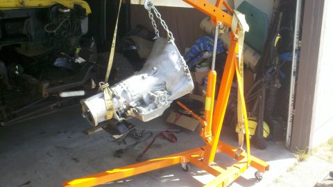 1978 Ford Bronco - A vehicle's transmission is being removed or installed using an engine hoist in a garage setting.