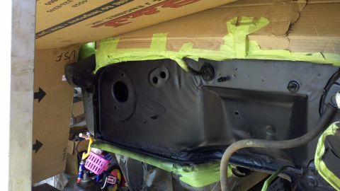 1978 Ford Bronco - The engine bay firewall is covered in black paint and green masking tape, with a cardboard box above and a tricycle below.