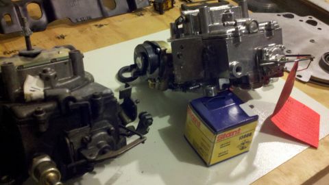 1978 Ford Bronco - Two carburetors and a box of parts are laid out on a workbench.