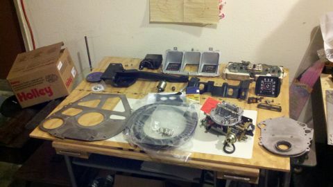 1978 Ford Bronco - A collection of engine parts, including a Holley carburetor and intake manifold, are laid out on a table, likely for a motor rebuild.