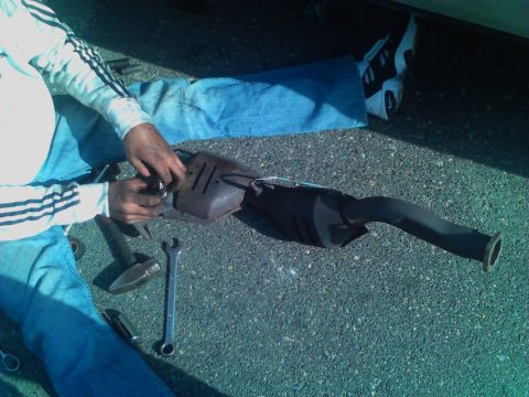 1999 Ford Crown Victoria - A person works on removing a vehicle's exhaust system components on the ground.