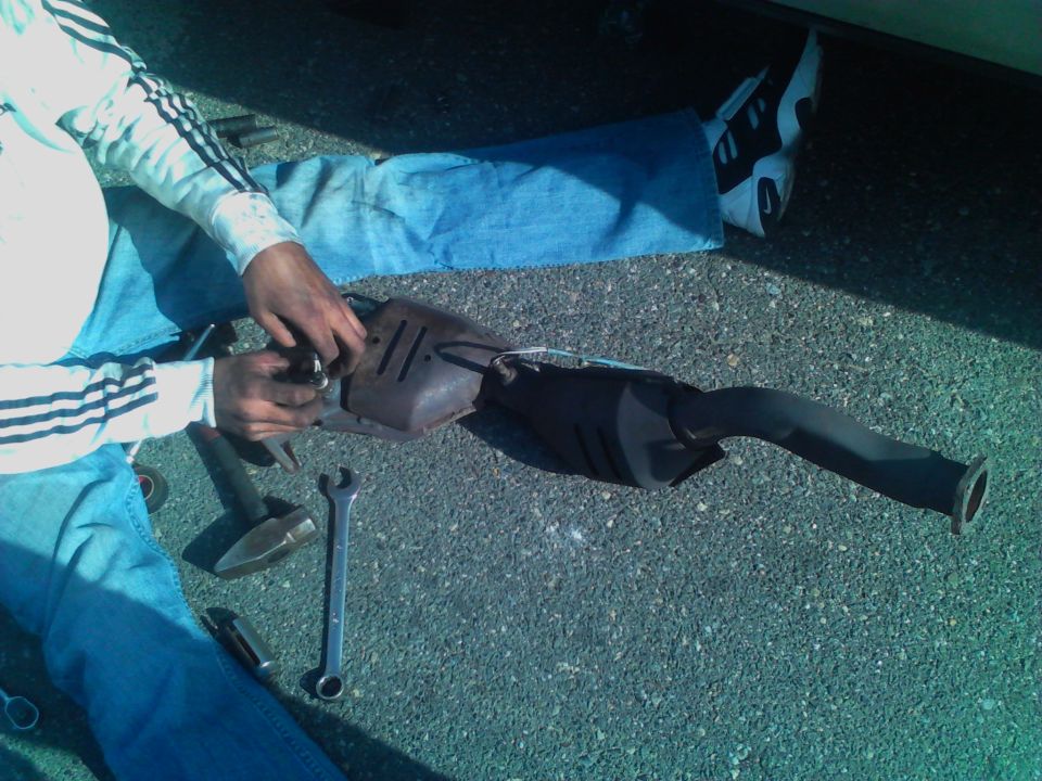 Exhaust pipe and catalytic converter removed from a vehicle, with tools on the ground