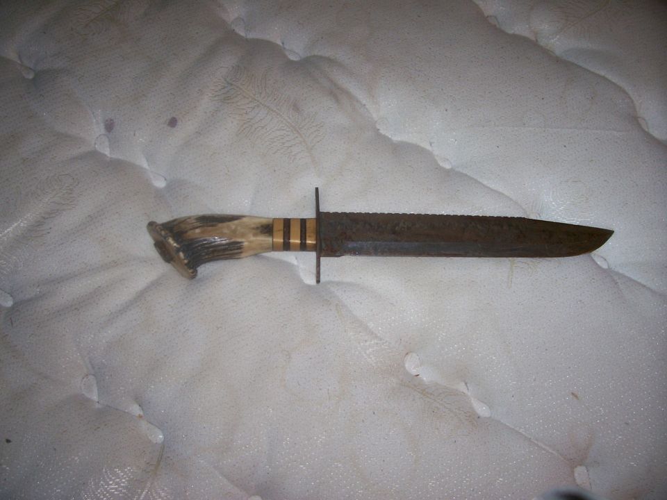 Hunting knife with antler handle and serrated blade on a white surface