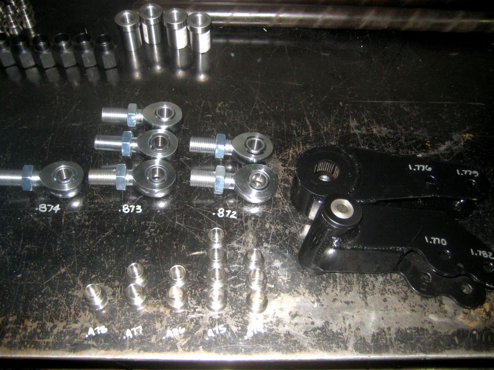 Assortment of rod ends, spacers, and black steering linkage components with part numbers