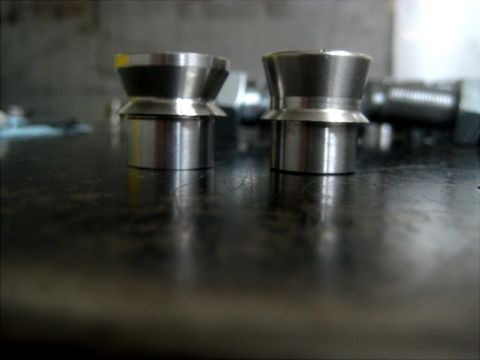 1996 Ford Bronco - Two metal parts with conical tops and cylindrical bases are shown on a dark surface.
