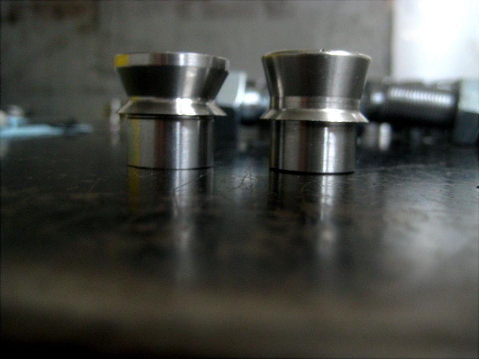 two metal conical parts with cylindrical bases on a dark surface