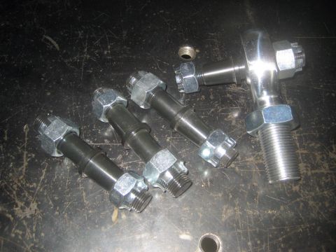 1996 Ford Bronco - Several chrome steering linkage rod ends and nuts are laid out on a dark, textured surface.