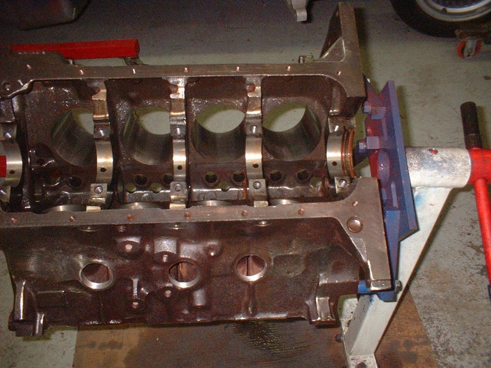 Bare V8 engine block on bench held in blue fixture, showing cylinder bores and main saddles