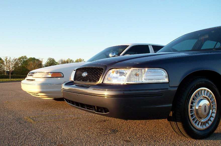 Dark blue Ford Crown Victoria front three-quarter view with white one behind at sunset