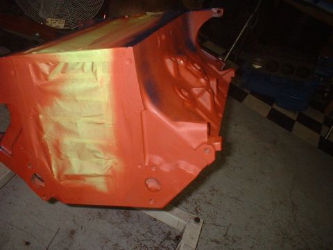 1957 Ford Custom Sedan - An engine block is shown being painted orange, with yellow masking tape applied to protect certain areas.