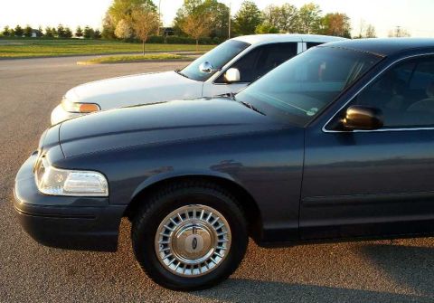1998 Ford Crown Victoria - Two Ford Crown Victorias are parked next to each other in a parking lot during the golden hour.