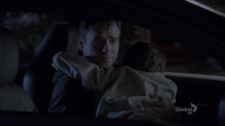 Man holding a child in a car interior at night. Text 'SHO' visible on headrest