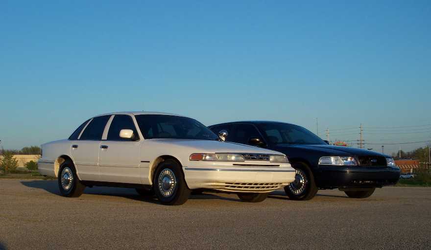 White and dark full-size sedans parked on asphalt lot under clear sky