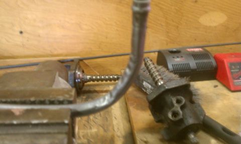 1978 Ford Bronco - A metal pipe is secured in a vise, with a brush tool and battery chargers in the background.