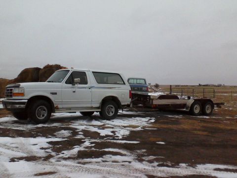 1994 Ford Bronco - White Ford Bronco towing a trailer with a blue pickup truck. The Bronco appears to be from the early to mid-1990s.