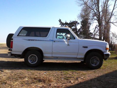 1994 Ford Bronco - This white Ford Bronco is shown from the side, parked outdoors with trees in the background.