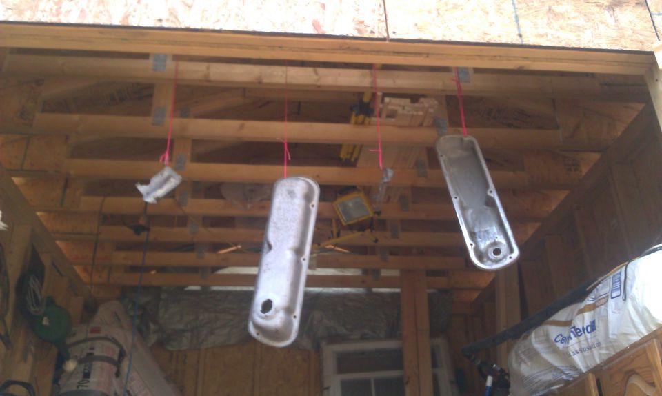 Two stripped metal valve covers hanging by pink string from garage ceiling joists