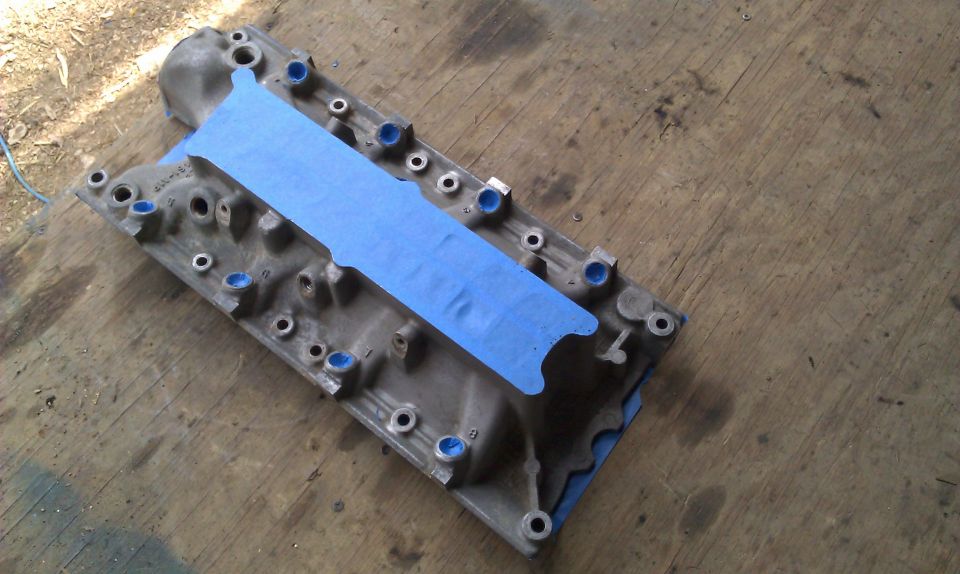 Cast aluminum V8 intake manifold on plywood with blue tape masking the valley and ports plugged