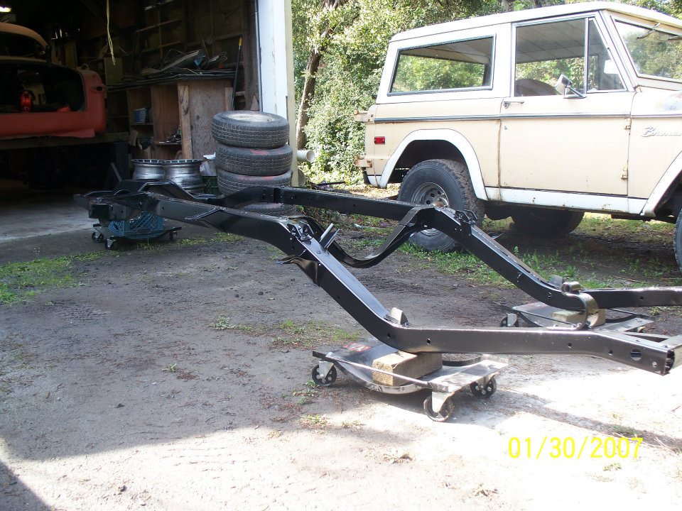 Tan 1978 Ford Bronco parked behind a black frame on dollies