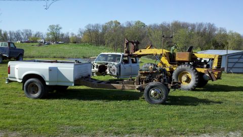 1993 Ford F-350 - A 1993 Ford F-350 truck chassis is shown with its engine and cab, being worked on with a large yellow machine.