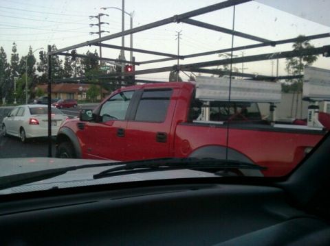 1988 Ford Bronco - A red pickup truck is seen in traffic, equipped with a rack system in its bed.