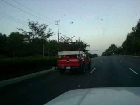 1988 Ford Bronco - A red pickup truck equipped with a ladder rack travels down a road under an overcast sky.