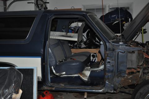 1986 Ford Bronco - The interior of a blue SUV is visible with the driver's side door open, revealing the seats and dashboard area.