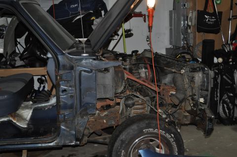 1986 Ford Bronco - Disassembled blue Ford Bronco with engine bay exposed and significant rust visible on the frame.