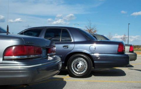 1998 Ford Crown Victoria - Two blue sedans are parked side-by-side under a bright blue sky.