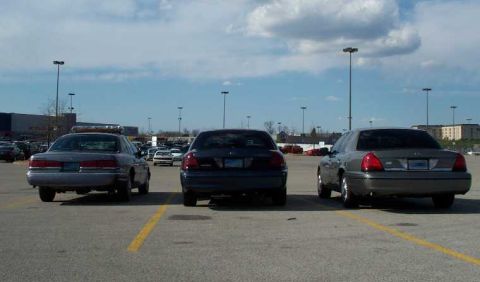 1998 Ford Crown Victoria - Three Ford Crown Victorias are parked in a lot under a cloudy sky.
