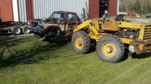 1993 Ford F-350 - A heavily rusted 1979 Ford pickup truck chassis is attached to a yellow front loader, parked on a grassy area next to a barn.