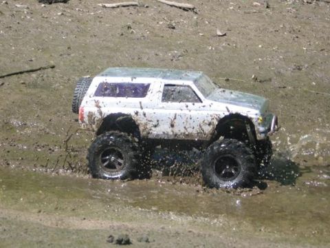 1986 Ford Bronco - This remote control monster truck is covered in mud as it navigates through a wet, muddy terrain.