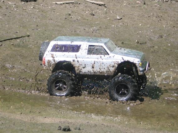 White remote control monster truck with large tires driving through mud