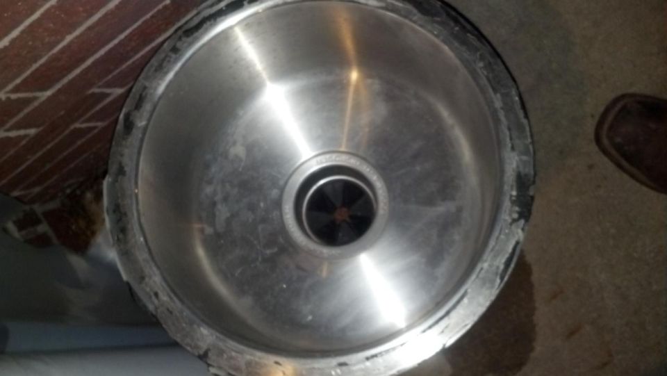 Close-up of a stainless steel kitchen sink drain with a black garbage disposal flange