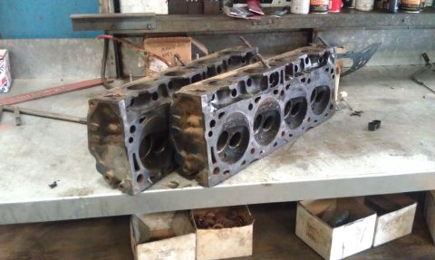 1978 Ford Bronco - Two engine cylinder heads are displayed on a workbench in a garage setting.