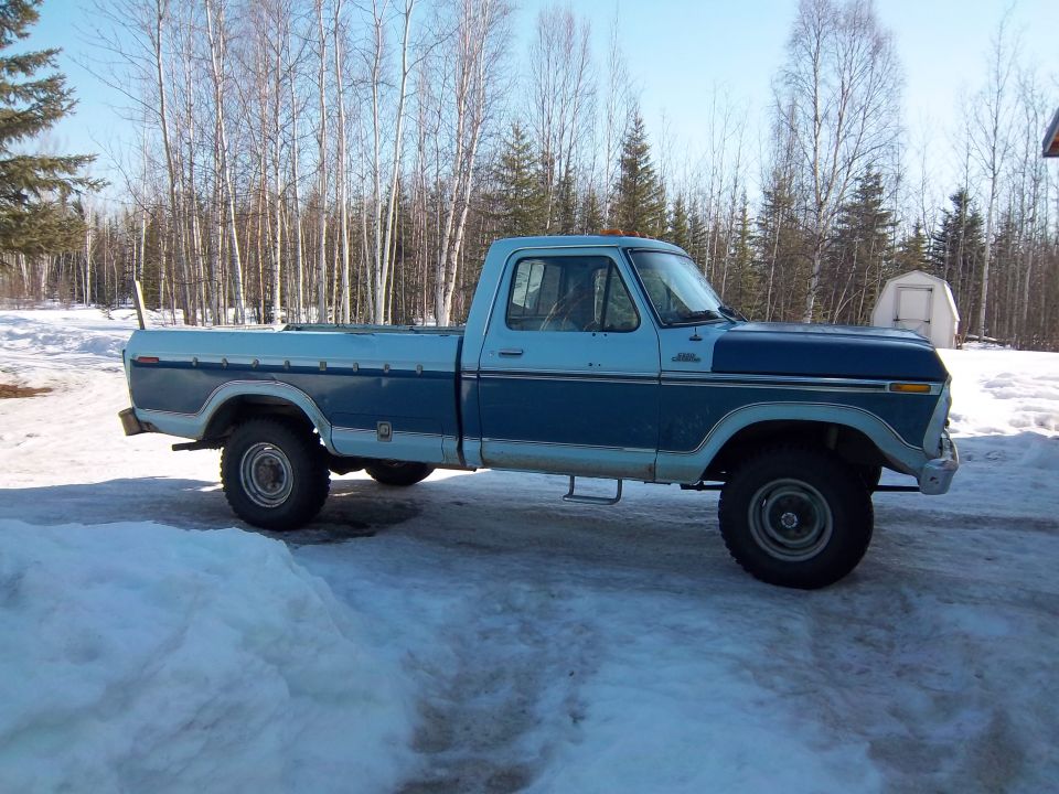 Blue and light blue Ford pickup truck parked in snow. It has a long bed and is lifted
